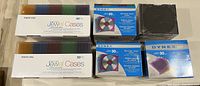Photo of two boxes of Memorex Ultra Clear jewel cases in assorted colors, two packs of Dynex slim jewel cases, and one pack of Dynex standard jewel cases, all sealed and new.