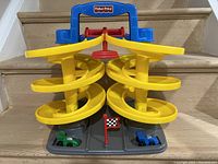 Fisher Price Little People Racing Garage with yellow spiral ramps, two race cars and checkered flag on gray base.