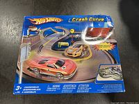 Front view of Hot Wheels Crash Curve toy set box showing racing cars, track, and included accessories. The box exhibits visible damage.