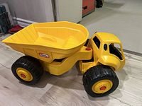 Side view of large yellow Little Tikes dump truck toy on floor showing wheels, cab, and dump bed