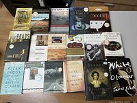 Photo showing 19 books from Oprah's Book Club, arranged on a wooden floor, titles visible including works by a variety of well-known authors.