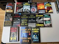 Photo showing 16 paperback thriller/mystery books by Lisa Gardner, James Patterson, David Baldacci, and Harlan Coben laid out on a table.