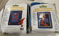 Photo of two Sesame Street Elmo junior throw blankets in original sealed packaging showing front labels with size and product details.