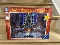 Front of Ravensburger 1000-piece Christmas ice skating nighttime puzzle box showing festive scene with ice rink, Christmas tree and city background.
