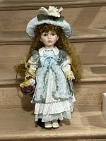 Full view of the porcelain Vanessa doll standing upright wearing detailed blue and white Victorian dress and bonnet.
