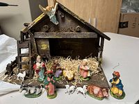 Overall view of the vintage nativity set with wooden stable and figurines arranged in front.