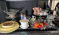 Overview of the collection including clear glass bowls and plates, milk glass planter, porcelain salt and pepper shakers shaped like pink pigs, small ceramic plates, glass fruit decorations, and some spice containers.
