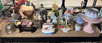Full view of porcelain, glass, and metal figurines, dishes, and containers on display including colorful and decorative small boxes and figurines.