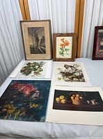 Six vintage art prints laid out on a table, including framed and unframed pieces with visible aging and discoloration.