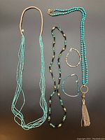 Full set of three long blue/turquoise beaded necklaces and two beaded bracelets on black background