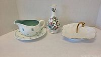 Three-piece ceramic lot including gravy boat with underplate, floral vase, and pickle dish with gold handle