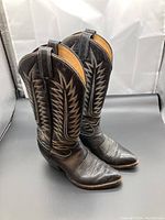 Pair of black Tony Lama cowboy boots angled side view showing overall design and shape, with visible pull tabs, stitching, and heel.