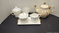 Full lot showing all pieces: Anchor cream and sugar set in front, Sango cream and sugar on tray in center, Sadler teapot on right.