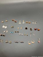 Multiple pierced earrings laid out on a black surface showing a variety of styles including studs, drop earrings, hoops, and dangles with metal and stone details