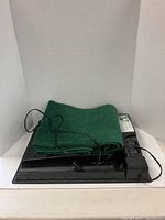 Electric indoor golf putting practice set laid out with coiled cord and green synthetic turf mat on black plastic base.