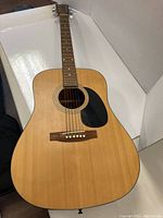 Full view of the acoustic guitar showing natural wood top with black pickguard and bridge with six strings.