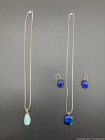 Two necklaces and one pair of earrings shown side by side, fused glass set and Larimar necklace