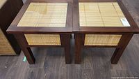 Two matching square end tables side by side showing the dark wood frame with glass tops and rattan inserts under the glass.