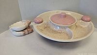 The main appetizer platter shows a beige speckled ceramic tray with three sections, a central pink lidded dip dish, and matching pink salt and pepper shakers on either side.