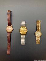 Three men's vintage wristwatches displayed side by side: left is a Recta watch with brown woven leather band; middle is a gold-tone Tradition automatic watch with silver metal band; right is a gold-tone Bill Blass watch with gold metal link bracelet.