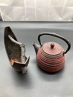 Photo showing the metal teapot and black flower vase side by side on a gray surface.