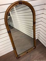 Front view of the rattan framed mirror showing the arched shape and brown rattan frame with darker rattan accents.