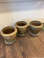 Group photo of three brown ceramic outdoor pots with matching saucers on wood floor