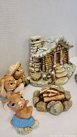 Ceramic log cabin with chimney, one bunny holding a fishing rod with hat, one bunny sitting in front with bucket on head