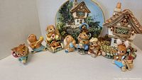 A group photo showing all 8 bunny figurines clustered together with the Cobble Cottage house and decorative plate in the background.