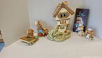 Photo showing the Pendelfin Castle Tavern house, bunny figurine in blue overalls, bulldog, and small bunnies grouped together.