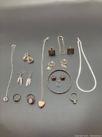 Top down view of assorted silver jewelry laid out on black background, including necklaces, earrings, rings, and bracelets.