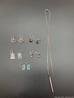 Full view of the necklace with bar pendant and all pairs of earrings on a grey background.