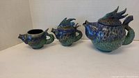 Front view of fish styled teapot, creamer, and sugar bowl set showing blue and green glaze and detailed scales and fins.