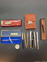 Photo showing 8 vintage pens in various colors and styles, shoe polishing kit in brown leather case, blue pen watch in box, and additional pen in a separate box.