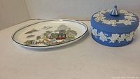 Full view of the oval platter with Asian-inspired scenic pattern and the round blue Wedgwood covered candy dish showing white relief decoration.