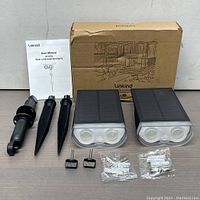 Full kit including two solar LED spotlights, two stakes, two small lights, mounting screws, and user manual with original box.