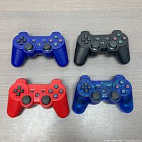 Four retro gaming controllers in blue, black, red, and transparent blue, placed on a wooden surface.