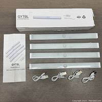 Four wireless LED closet lights with motion sensors, four USB charging cables, instruction manual and product box GYTL on a brown surface.