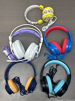 Bundle of five wired headphones in various colors and styles arranged on a flat surface.