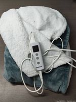 Electric heated blanket folded showing soft plush and sherpa-like layers with attached wired controller.