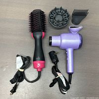 Overview of the purple hair dryer and black and pink hot air brush with power cords and diffuser and concentrator attachments