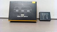 HDMI KVM switch device next to its original packaging box on plain surface.