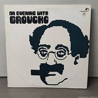 Front cover of the vinyl LP, white background with a stylized black graphic image of Groucho Marx's face with his signature glasses, mustache, and cigar, with the title 'AN EVENING WITH GROUCHO' in bold letters.