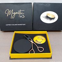 Two unopened magnetic eyelash kits displayed in black and yellow boxes containing eyelashes, eyeliner, small mirror, and eyelash curler with rose gold handles.