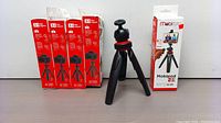 Five boxed Mobipod TT25 tripods and one unboxed tripod set up showing its compact design and flexible legs with red accents.