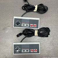 Pair of classic Nintendo NES style retro wired controllers with cables coiled and tied with rubber bands.
