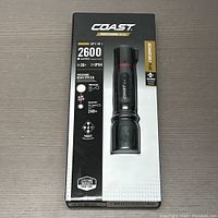 Coast XP11R flashlight in packaging showing 2600 lumens, IP54 rating, focusing beam system, 4 lighting modes, and included rechargeable battery.