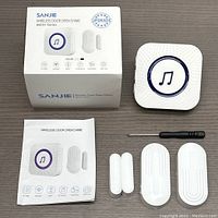 Photo of box, chime unit, magnetic sensors, screwdriver, and user manual laid out on table illustrating all included items.