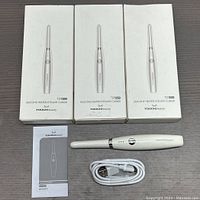 Three boxed silicone heated eyelash curlers, one unboxed curler, USB charging cable and instruction manual laid out on table.