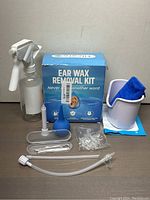 Photo of all kit components arranged in front of the box including spray bottle, blue bulb, irrigation syringe, ear basin with blue cloth, container with ear picks and tweezers, and silicone caps